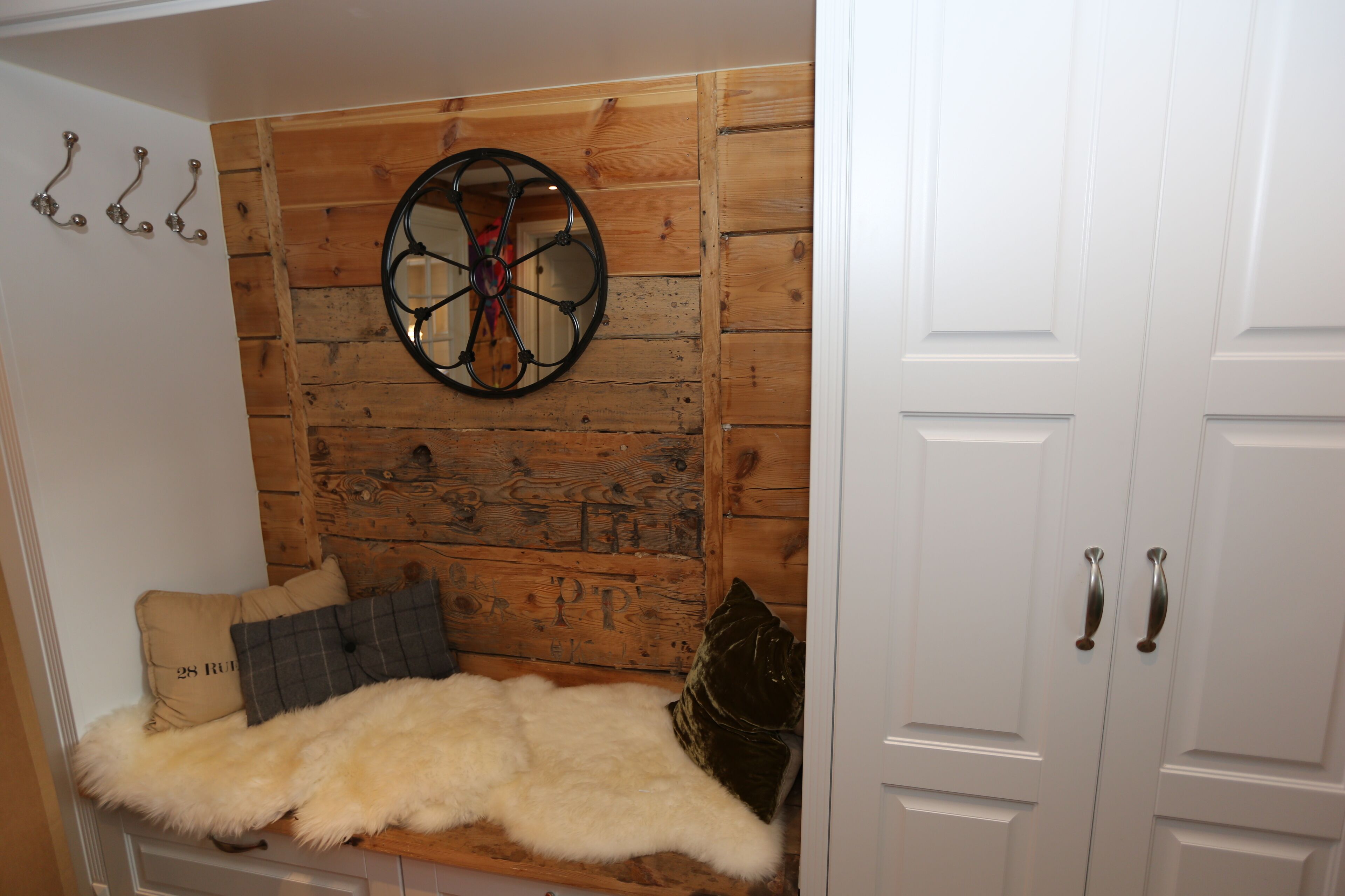 Ett rum med en väggpanel av trä, en rund spegel, en fäll av fuskpäls och en bänk.