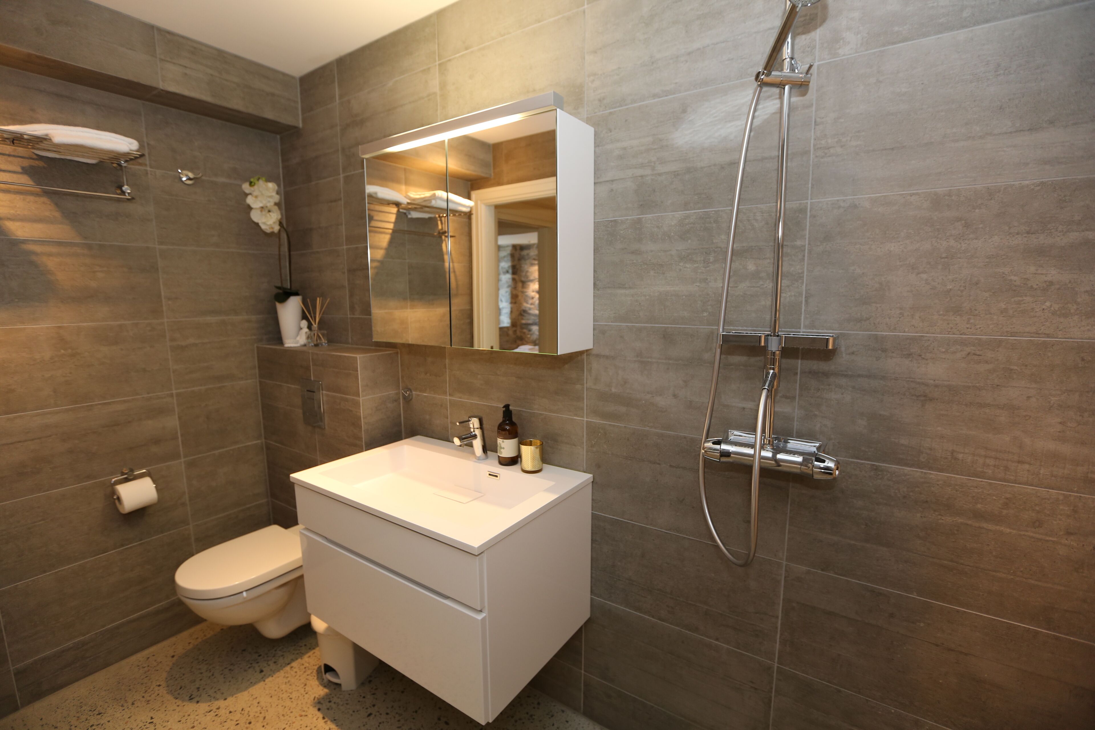 A modern bathroom with a white vanity, a large mirror, a shower, and a toilet.