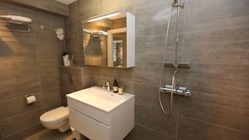 A modern bathroom with a white vanity, a large mirror, a shower, and a toilet.