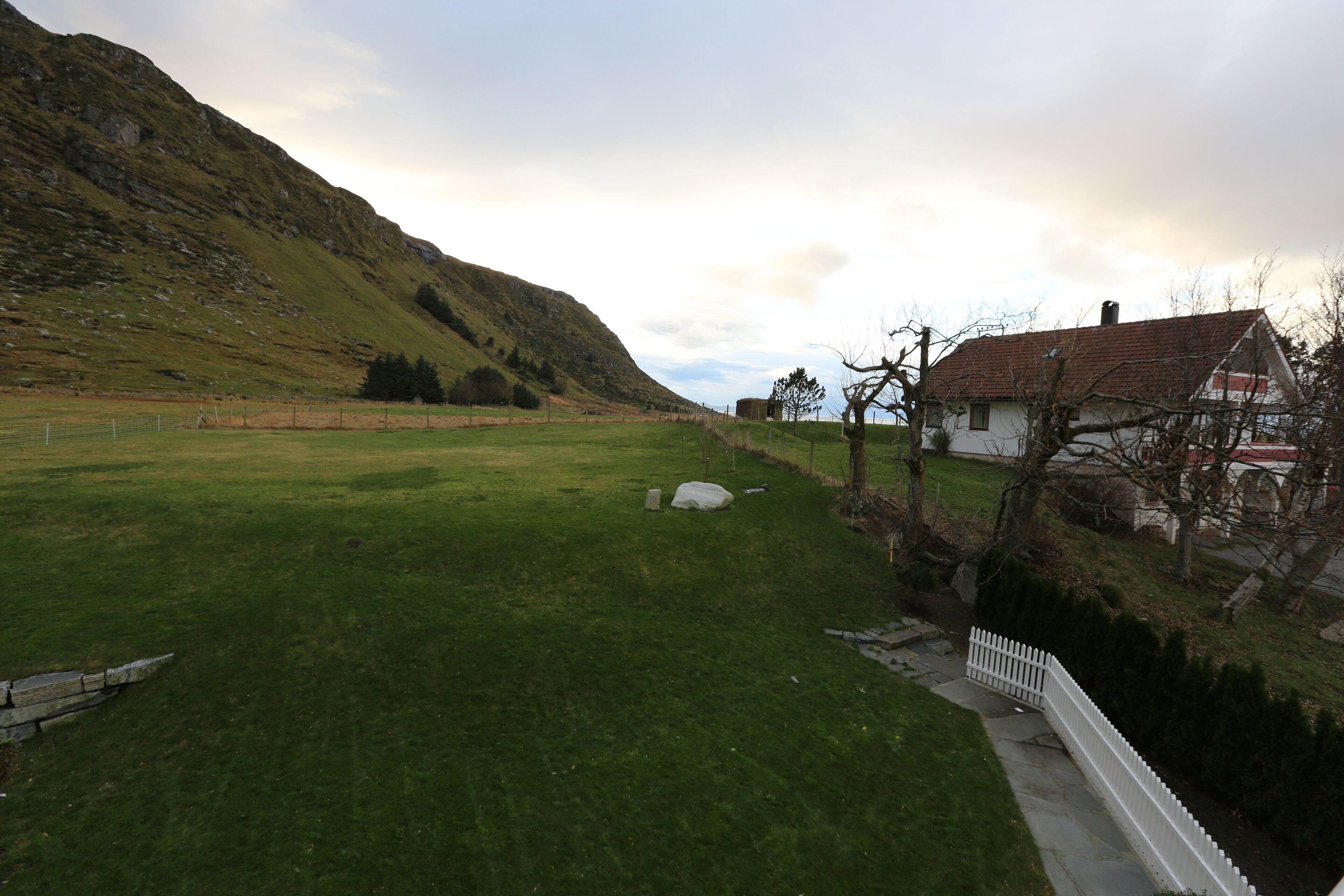 A rural landscape with a house, a grassy field, and a hill.