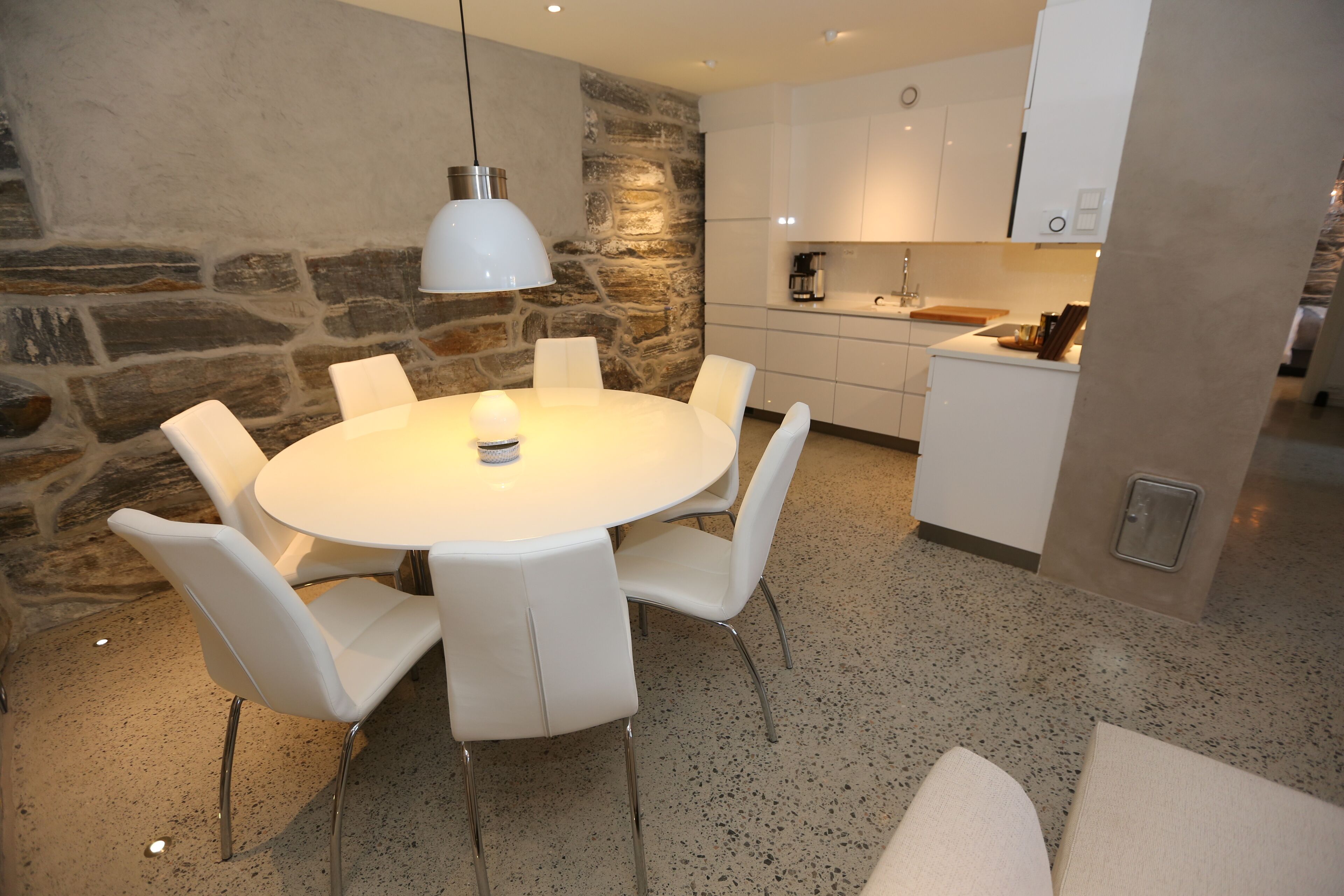 Una cocina moderna con armarios blancos, una pared de acento de piedra y una mesa de comedor redonda con sillas blancas.