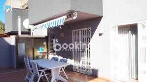 An outdoor patio with a white table and chairs, a striped awning, and a metal gate. - APARTMENT WITH 3 ROOMS AND LARGE TERRACE, 5 MIN. FROM THE BEACH, IN THE CENTER (Platja d'Aro)