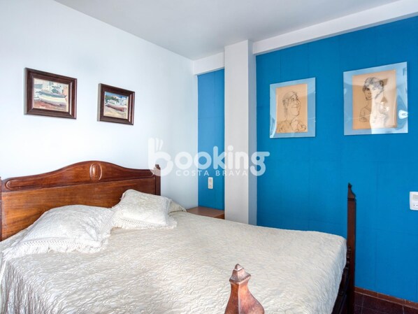 A bedroom with a wooden bed, white bedding, and blue walls. There are two framed pictures on the wall. - APARTMENT AT THE FIRST LINE OF SEA WITH SPECTACULAR SEA VIEWS (Platja d'Aro)