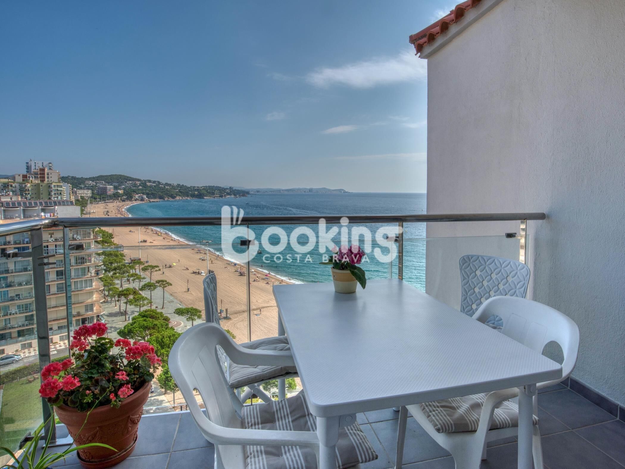A balcony with a white table and chairs, overlooking a beach and ocean.