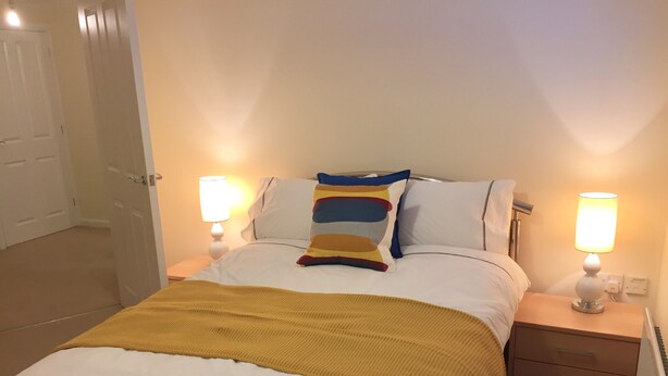 A neatly made bed with a yellow throw blanket, two bedside lamps, and a wooden nightstand with drawers. - Modern 2 Bed Apartment in Southampton (Southampton)