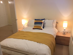A neatly made bed with a yellow throw blanket, two bedside lamps, and a wooden nightstand with drawers.