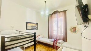 A dormitory room with bunk beds, a single bed, a desk, a chair, a television, a painting, a window with curtains, and a ceiling light. - Comfort Inn Roma Termini (Rome)