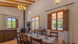 A dining area with a wooden table, chairs, and a chandelier. There is a sofa and a window with curtains. - Villa with detached house, air conditioning, wifi, garden, private swimming pool (Santa Margalida)