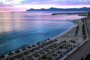 A beach with rows of sun loungers and thatched umbrellas, a pier with boats, and mountains in the background. - Villa with detached house, air conditioning, wifi, garden, private swimming pool (Santa Margalida)