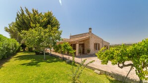 A rustic stone house with a tiled roof, surrounded by lush greenery and a well-maintained lawn. - Villa with detached house, air conditioning, wifi, garden, private swimming pool (Santa Margalida)