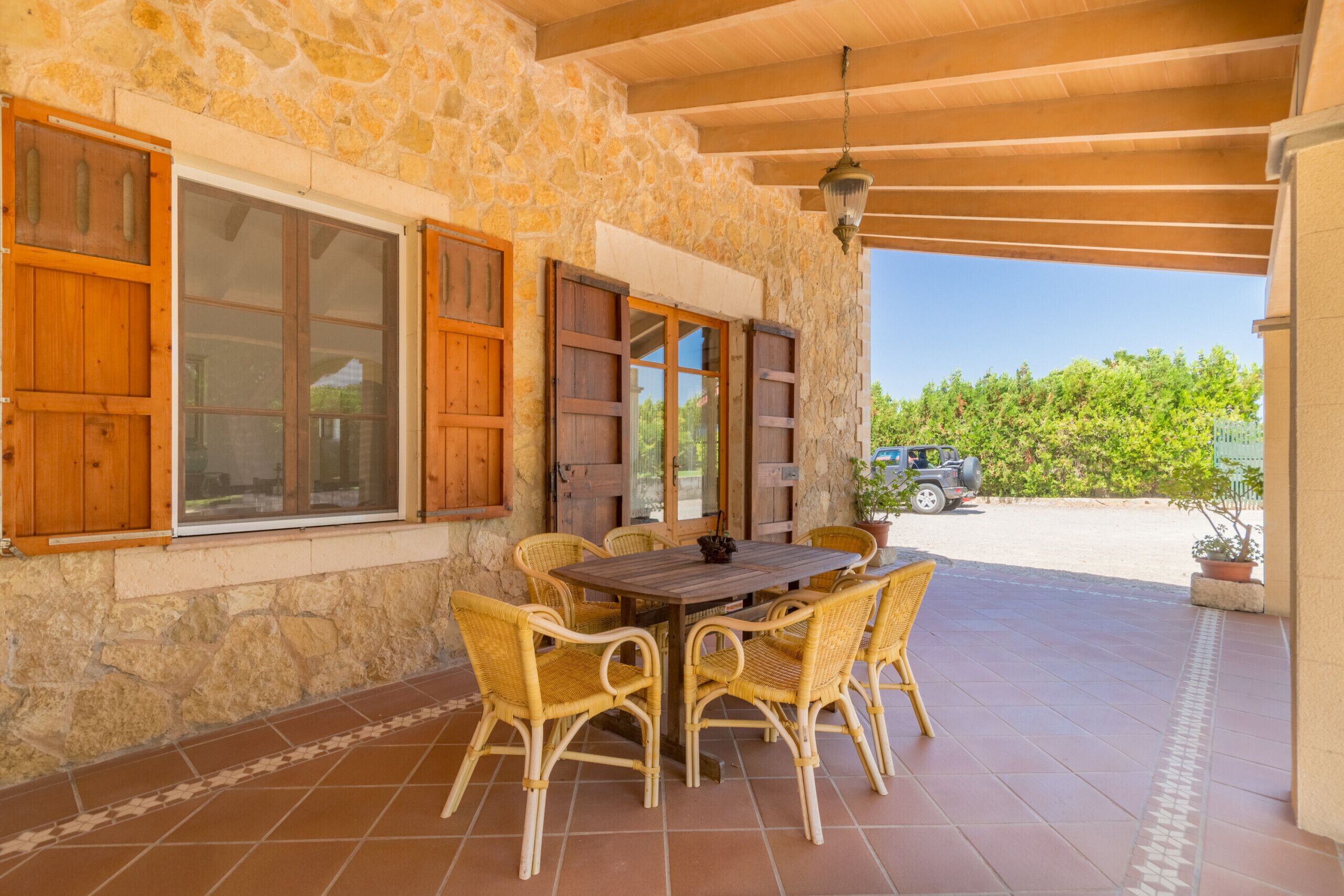 An outdoor patio with a stone wall, wooden shutters, a table with chairs, and a hanging light fixture.