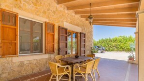 An outdoor patio with a stone wall, wooden shutters, a table with chairs, and a hanging light fixture. - Villa with detached house, air conditioning, wifi, garden, private swimming pool (Santa Margalida)