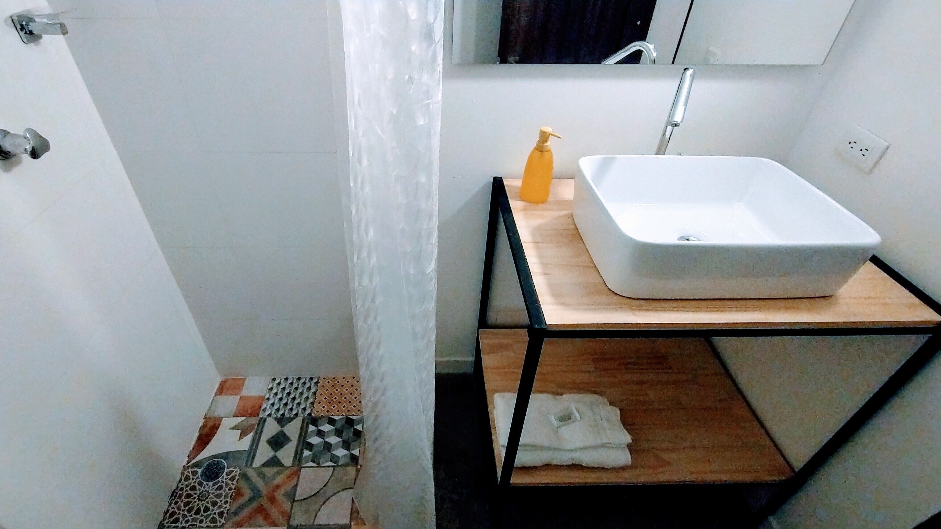 Een badkamer met een wit wastafel, een houten plank en een vloer met patroon.