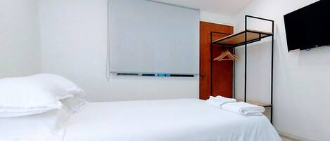 A hotel room with a bed, a wooden door, a coat rack, and a flat-screen TV mounted on the wall.