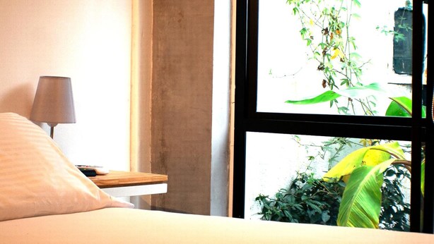 A bedroom with a bed, a bedside table with a lamp, and a window with a view of greenery. - Casa SAB  Los Andes (Bogotá)