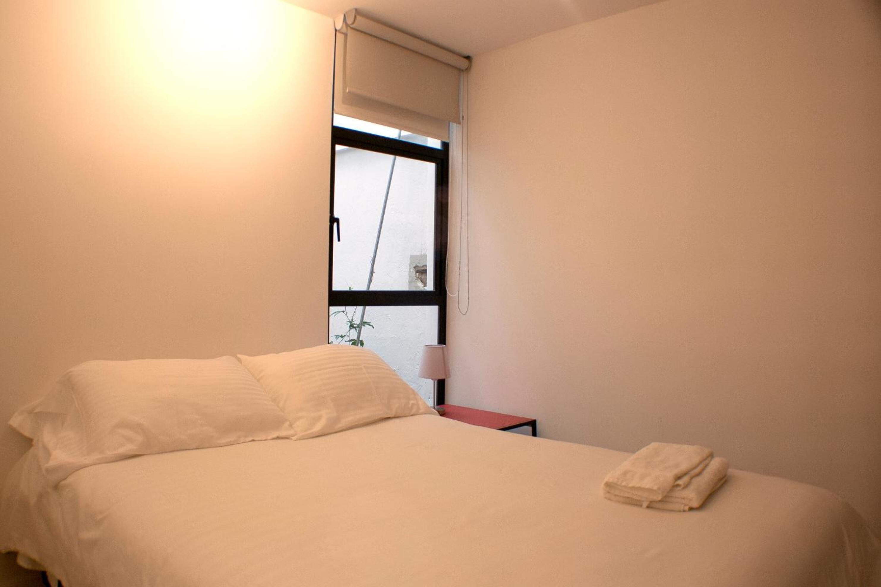 A bedroom with a bed, a nightstand, a lamp, and a window with a view.