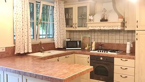 Een keuken met een centraal kookeiland, een magnetron, een fornuis en barstoelen.