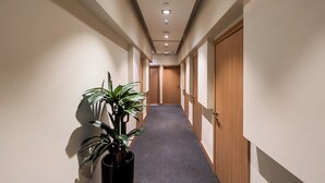 A hallway with a carpeted floor, wooden doors, and recessed ceiling lights. - Sleepover Terminal 1, Concourse D – formerly sleep ‘n fly (Dubai)