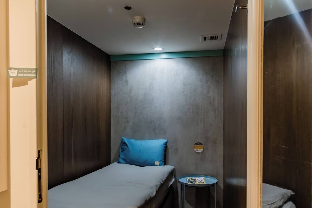 Una habitación compacta con una cama, una mesita redonda pequeña y una lámpara fijada a la pared.