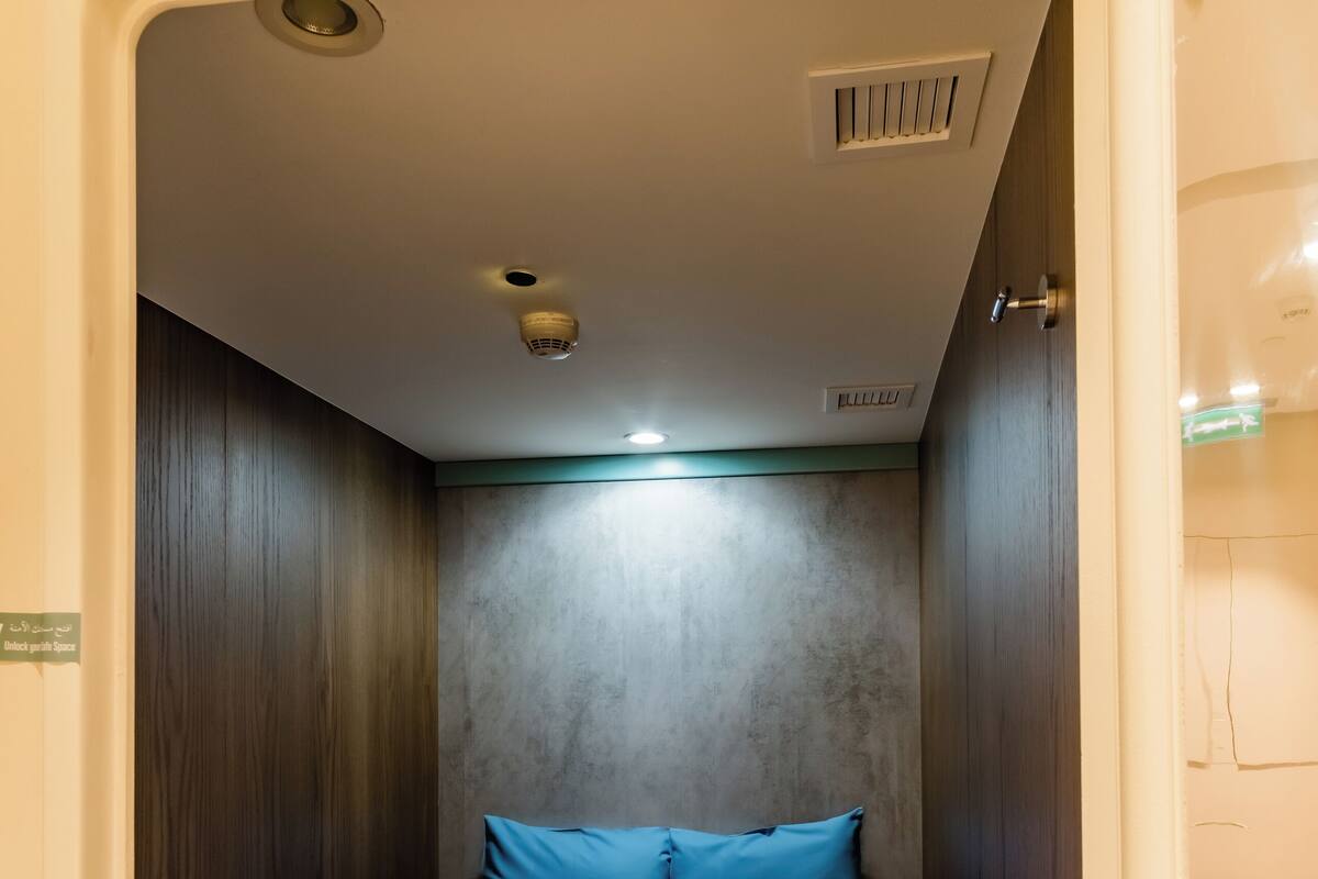 Habitación pequeña con una cama individual, una mesita de noche y una lámpara fijada a la pared.