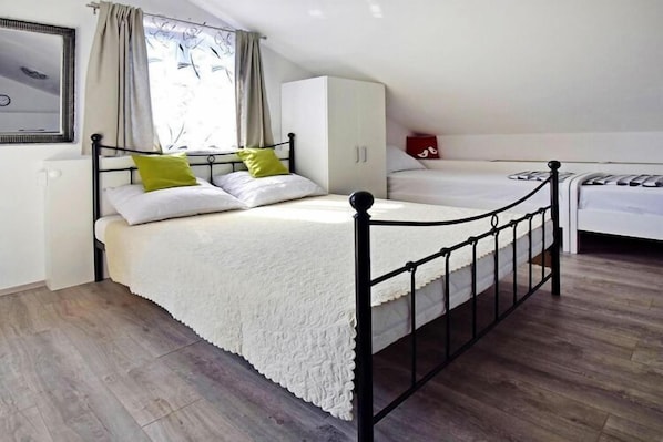 A single bed with a white duvet and a black metal frame, a white wardrobe, and a window with curtains.
