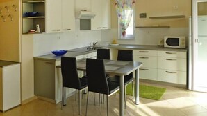 A compact kitchen with white cabinets, a microwave, a sink, and a dining area with four chairs.