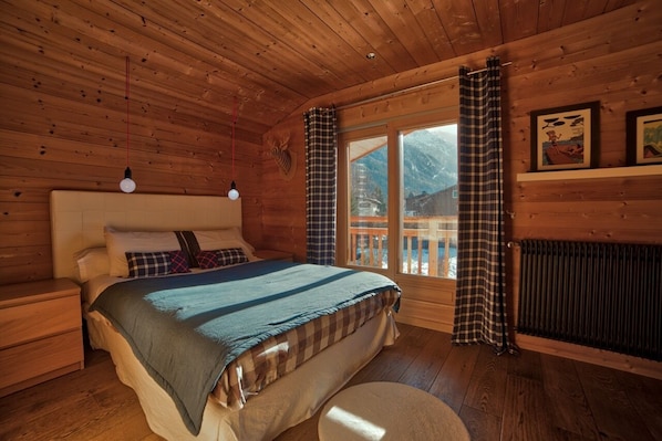 A cozy wooden cabin bedroom with a large bed, a window with a view of a mountain, and a radiator.