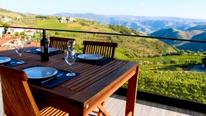 Una mesa de madera con platos, vasos y una botella, con vistas a un paisaje pintoresco con colinas y un valle.