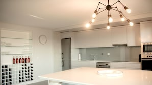 Una cocina moderna con una isla central, armarios blancos y una vinoteca con botellas.