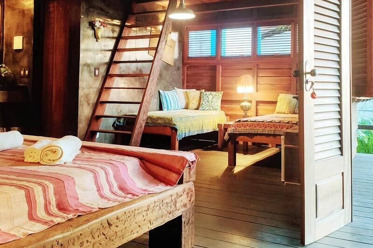 Une chambre à coucher accueillante, aménagée dans le style d’un chalet, avec un grand lit, deux petits lits, une échelle et un escalier en bois.