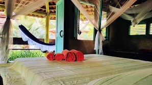 A bed with rolled red towels, a green door, and a window with a view of greenery. - Convento Arcádia (Barreirinhas)