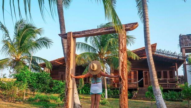 A person standing under a wooden structure with palm trees in the background. - Convento Arcádia (Barreirinhas)