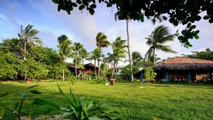 A tropical garden with palm trees, a thatched-roof hut, and a well-maintained lawn. - Convento Arcádia (Barreirinhas)
