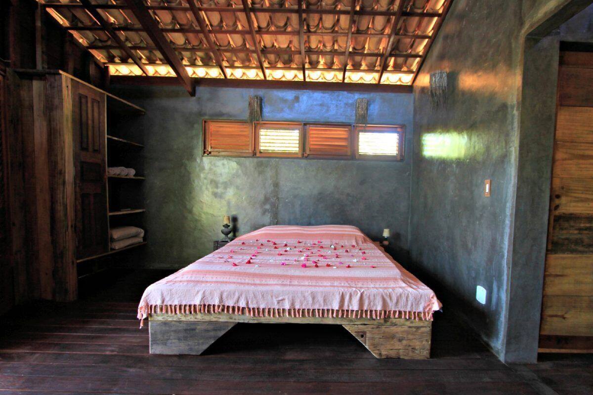 Une chambre avec un lit en bois, une étagère avec des serviettes et une fenêtre avec des stores.