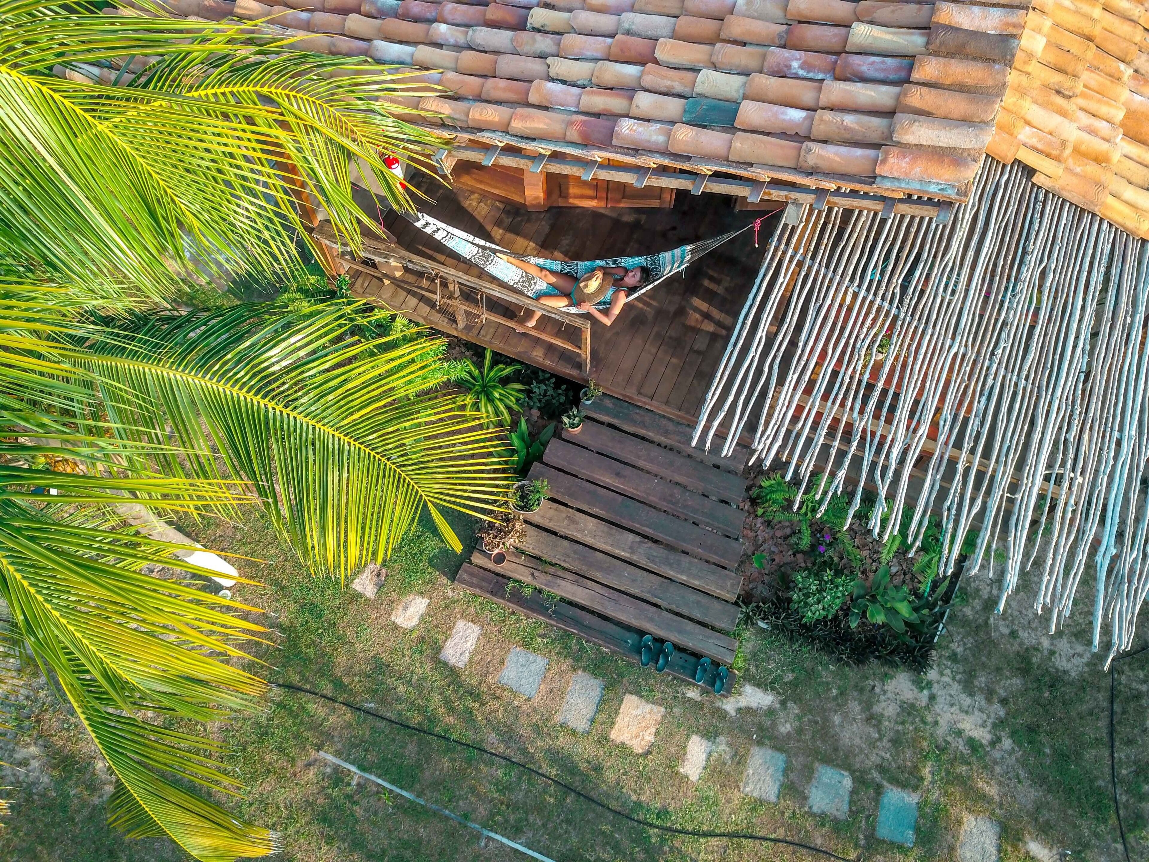 Un hamac sous un toit de tuiles, entouré d’une terrasse en bois et de palmiers.