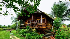 A wooden cabin with a porch, surrounded by lush greenery and a stone pathway leading to the entrance. - Convento Arcádia (Barreirinhas)