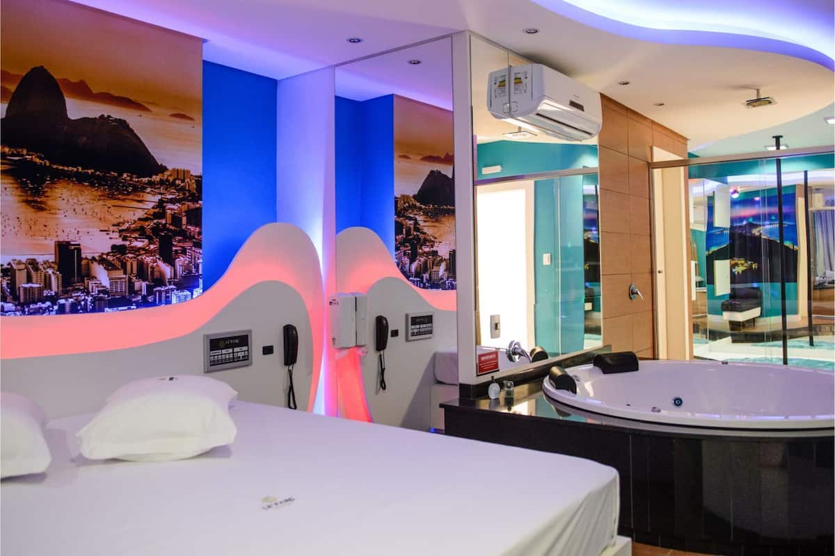 A modern hotel room with a bed, a large window, a jacuzzi, and a cityscape mural on the wall.