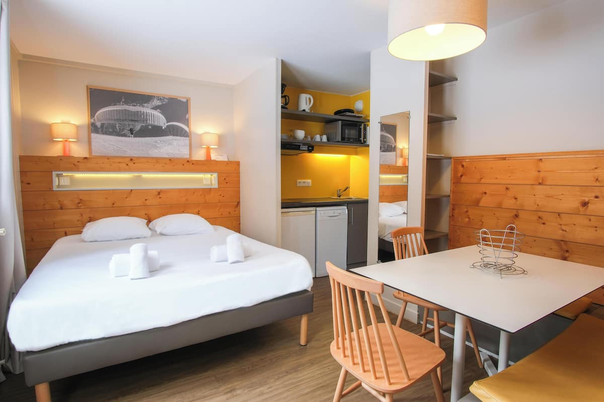 Ein Hotelzimmer mit Bett, Nachttischlampen, einem Tisch, Stühlen, einer Mikrowelle und einer kleinen Küchenzeile.
