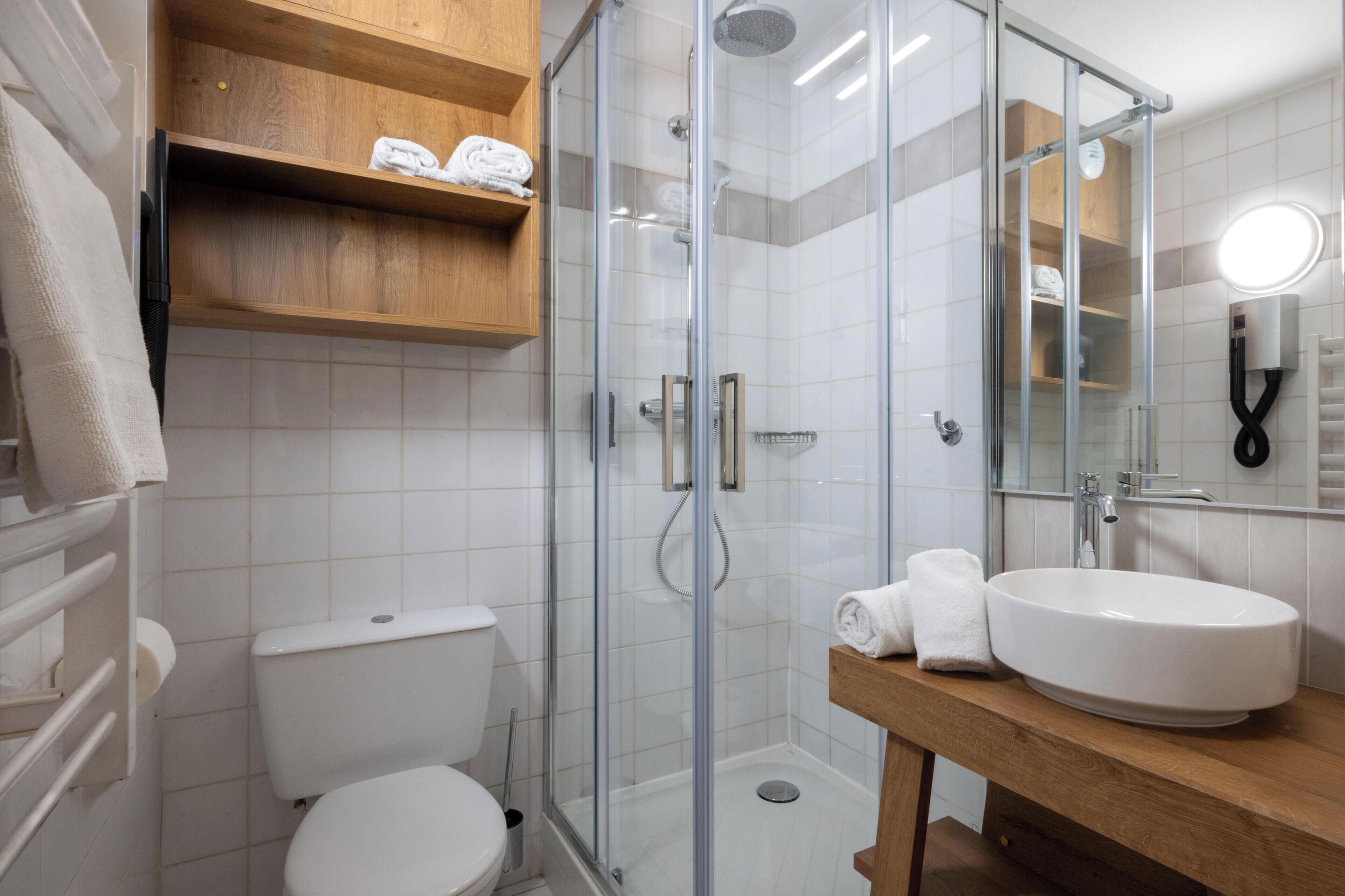 A modern bathroom with a glass shower enclosure, a white toilet, a wooden vanity with a sink, and a towel rack.