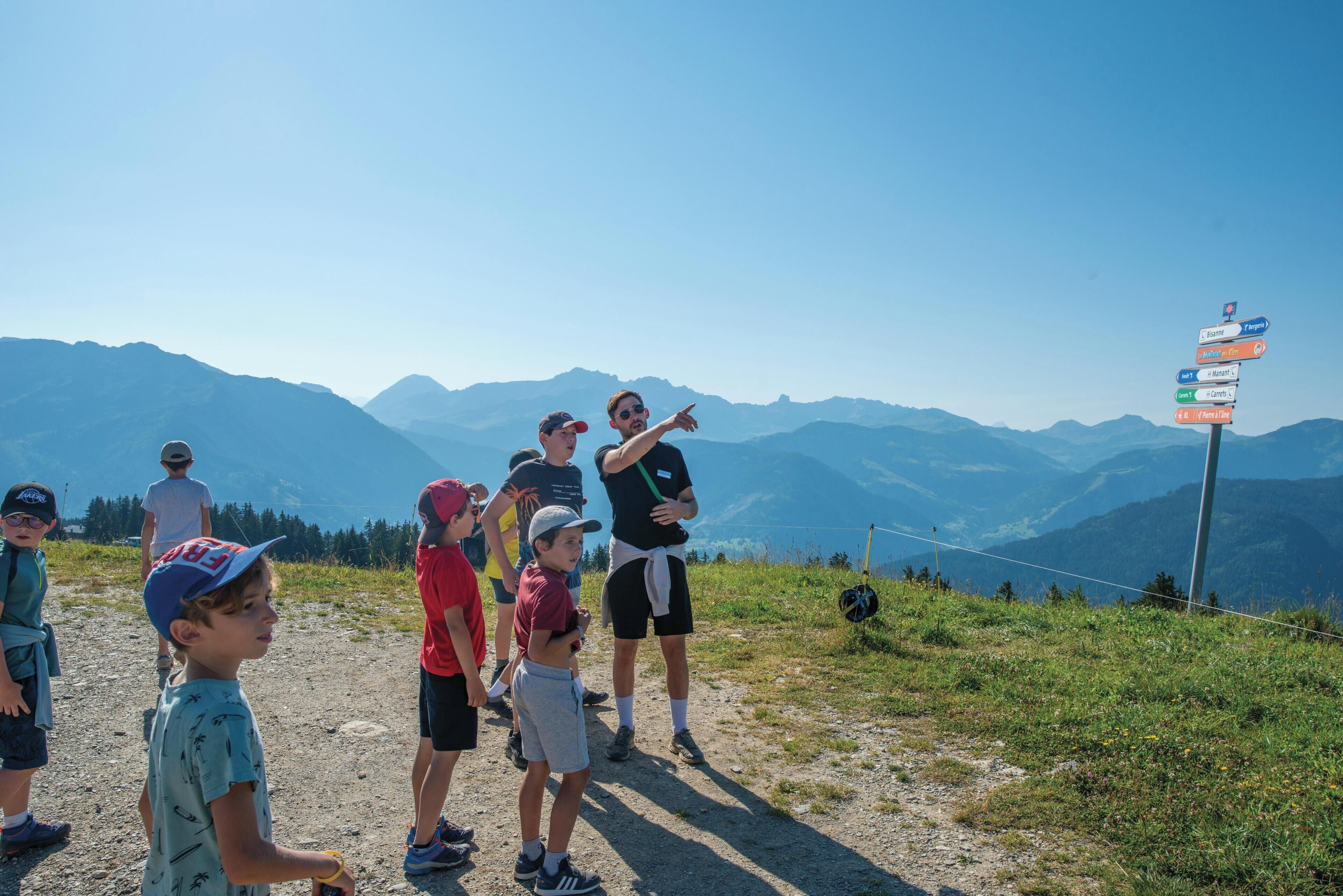 A group of people standing on a mountain trail with a signpost indicating directions to various locations.