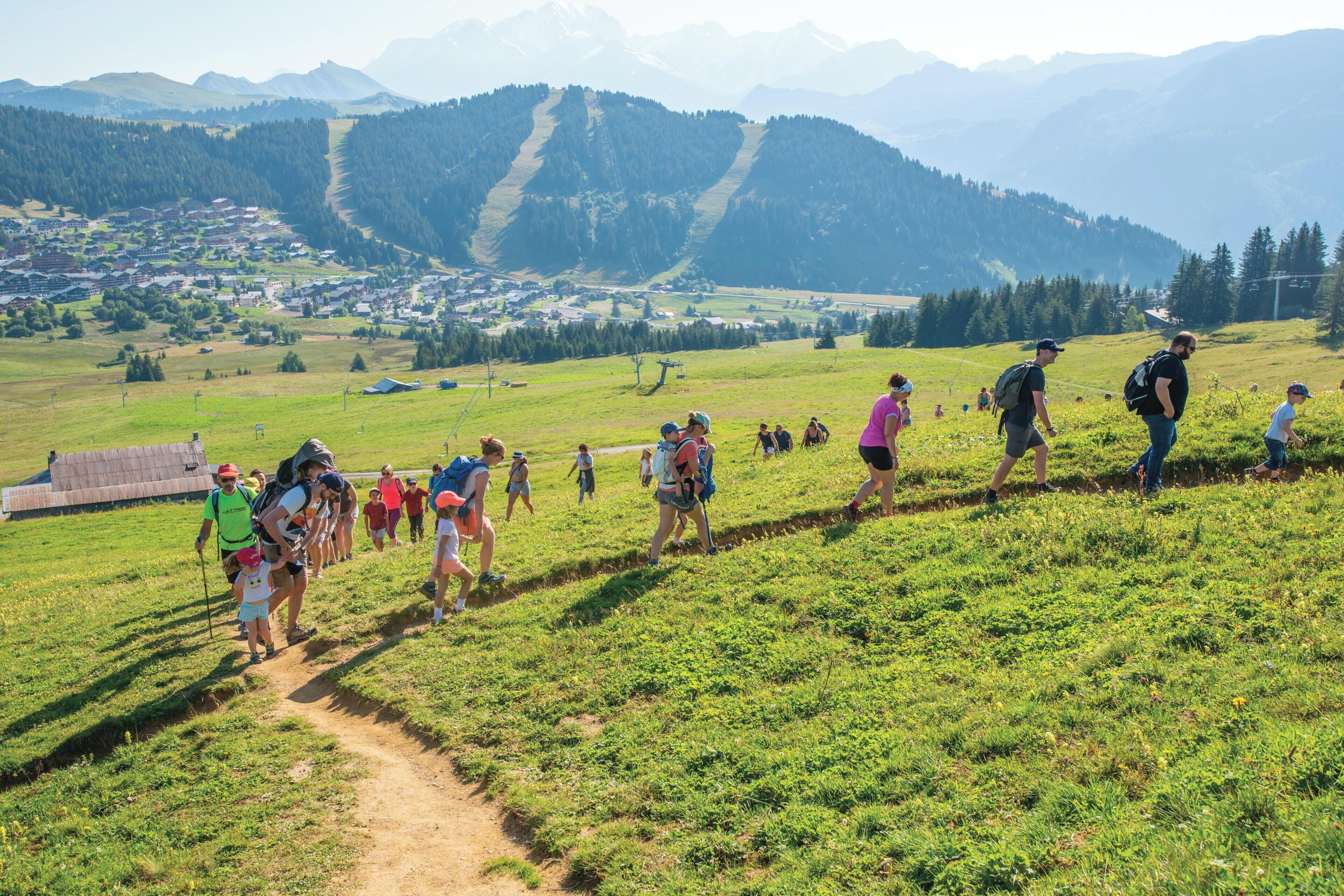 A group of people hiking on a dirt path in a grassy field with mountains in the background.