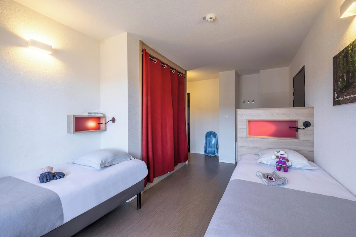 Ein Hotelzimmer mit zwei Betten, einem roten Vorhang, einem blauen Rucksack und einem Bild an der Wand.