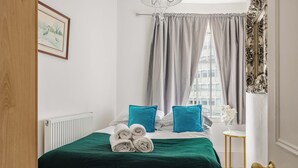 A neatly made bed with teal pillows, a green bedspread, and rolled towels on the side. - 3-bedroom apartment Lancaster gate (London)