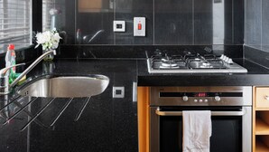 A modern kitchen with a stainless steel sink, a gas stove, an oven, and a black tiled backsplash. - 3-bedroom apartment Lancaster gate (London)