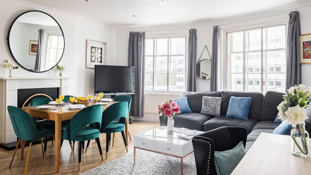 A modern living room with a dining area, large windows, and a fireplace. - 3-bedroom apartment Lancaster gate (London)