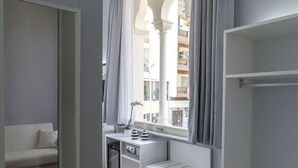 Una habitación moderna con piso de madera, un escritorio blanco, un sofá blanco y un amplio ventanal con cortinas.