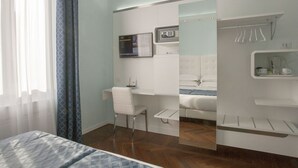 Habitación de hotel con cama, escritorio, espejo, zona de ducha y perchero.