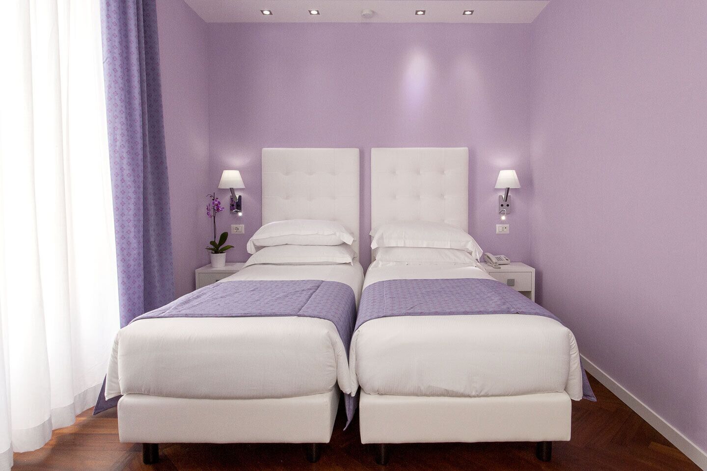Une chambre double avec deux lits, du linge de lit blanc, des touches de couleur violette et des lampes de chevet.
