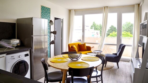 A compact kitchen with a washing machine, a refrigerator, and a dining area with a round table and chairs. - 4 bedroom apartment on the outskirts of Rouen (Rouen)