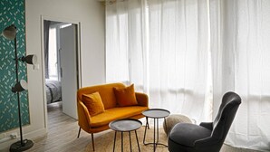 A room with a sofa, armchair, and two small tables. There is a door leading to another room and a patterned wall. - 4 bedroom apartment on the outskirts of Rouen (Rouen)